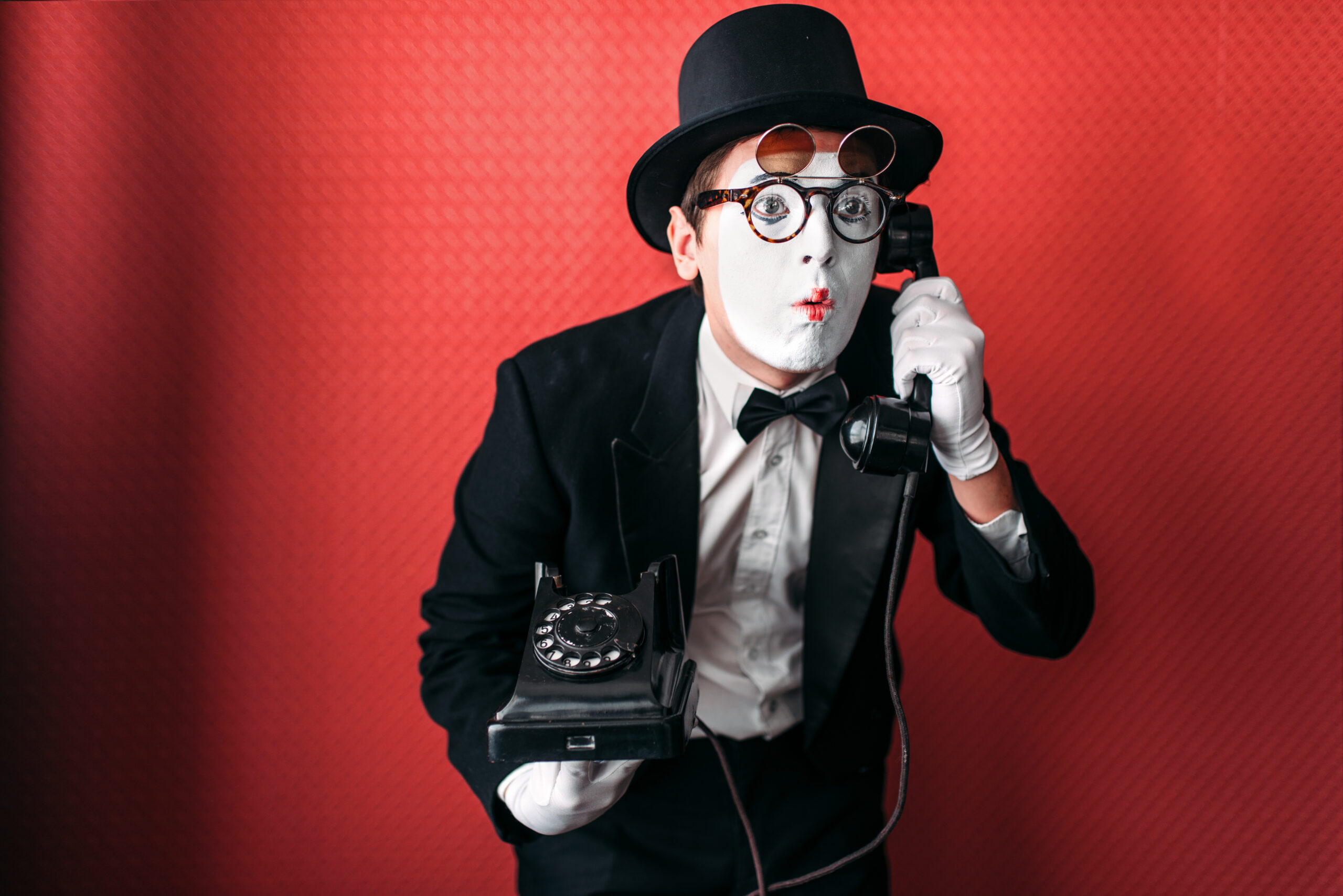 Mime theater actor performing with old telephone. Comedy pantomime artist in suit, gloves and hat